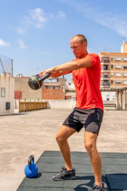 Kafkasyalı genç adam sokakta çan ağırlıklarıyla çömeliyor forma girmek ve vücudu hakkında iyi hissetmek için antrenman yapıyor. Sağlıklı yaşam konsepti