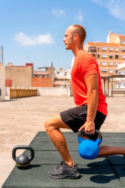 Beyaz bir genç çan ağırlığıyla kol egzersizi yapıyor, arkası dönük. Eğitim kavramı