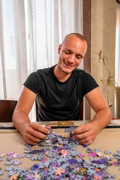 Adolescent attrayant dans un t-shirt noir assemblant un puzzle dans le salon à la maison. Concept de formation — Photo