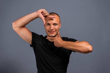 Gülümseyen sıradan bir adamın portresi Gri arka planda elleri olan bir çerçeve yapıyor