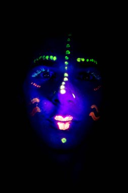 UV ışığıyla parıldayan partide yüzü boyanmış genç bir çocuk.