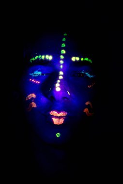 UV ışığıyla parıldayan partide yüzü boyanmış genç bir çocuk.