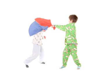 Küçük çocuklar pijamalarıyla beyazlar içinde yastık savaşı yapıyorlar.