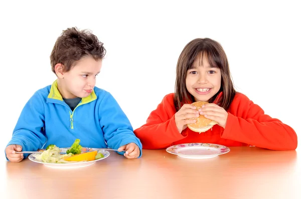 Niño y niña comiendo hamburguesa y verduras — Foto de Stock