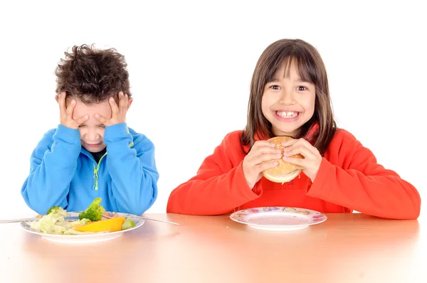 Menino e menina comendo hambúrguer e legumes — Fotografia de Stock