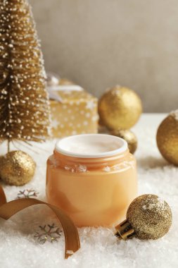 Arka planda dekoratif karlı kozmetik krem ve Noel aksesuarları var.