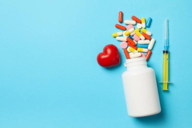 Mavi arka planda plastik şişe, hap, şırınga ve kalp.