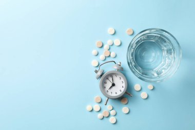 Bir bardak su, çalar saat ve mavi arka planda haplar.