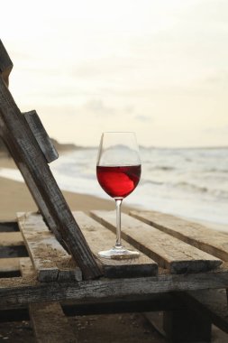 Kumlu deniz sahilinde bir bardak şaraplı ahşap bank.