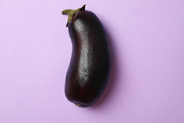 Fresh raw eggplant with water drops on violet background