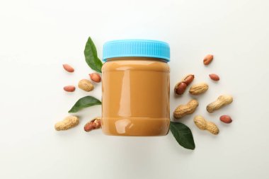 Fıstık ezmeli kavanoz, fıstık ve yapraklar beyaz arka planda.