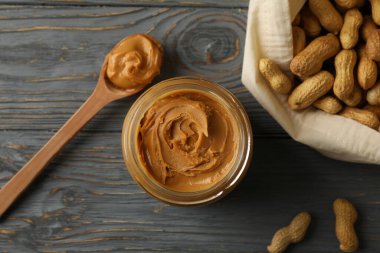 Fıstık ezmeli kaşık ve kavanoz ve tahta arka planda fıstık ezmesi ve poşet.