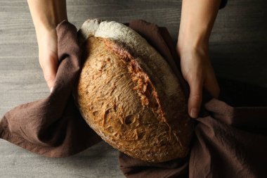 Peçeteli kadın elleri gri arka planda taze ekmek tutuyor.