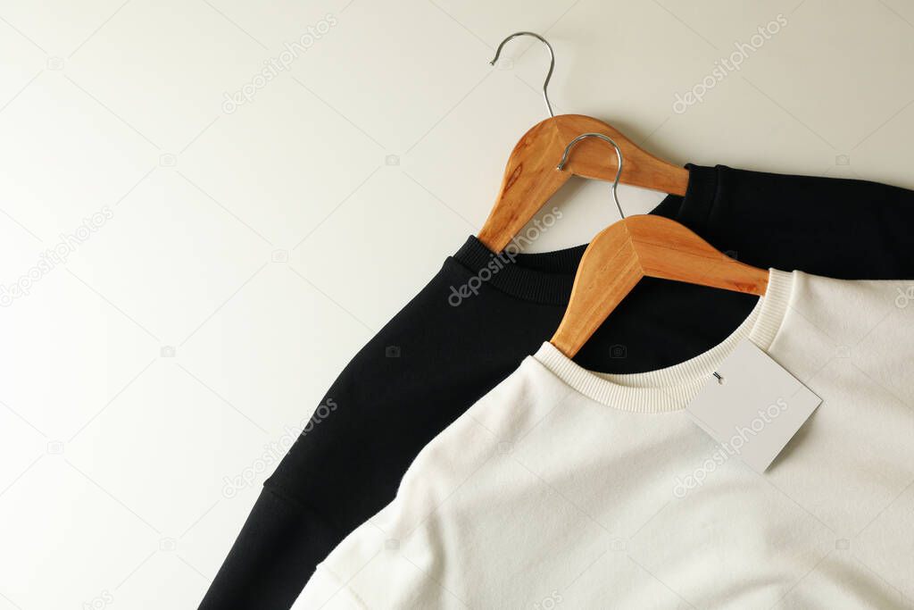 Hangers with stylish sweatshirts on white background