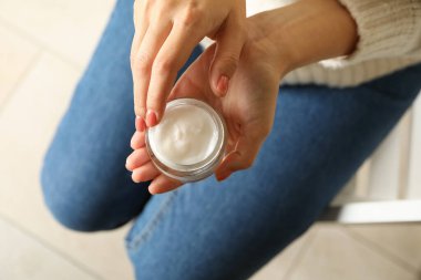 Kazaklı ve kot pantolonlu kadın kozmetik krem kavanozu tutuyor.