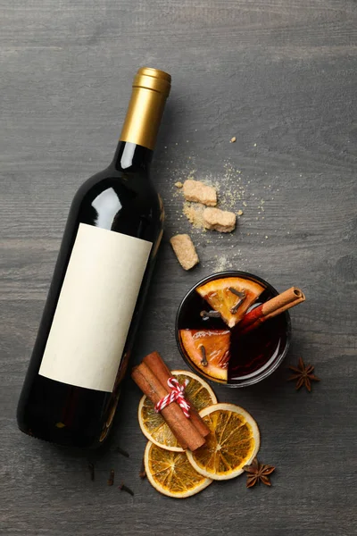 Bottle of wine, cup of mulled wine and ingredients on wooden background