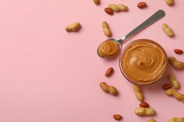 Fıstık, kase ve kaşık pembe arka planda fıstık ezmeli.