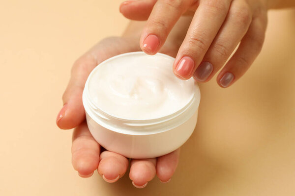 Cute female hands hold jar of cosmetic cream on beige background
