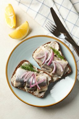 Beyaz desenli arka planda taze ringa balıklı bir tabak sandviç.