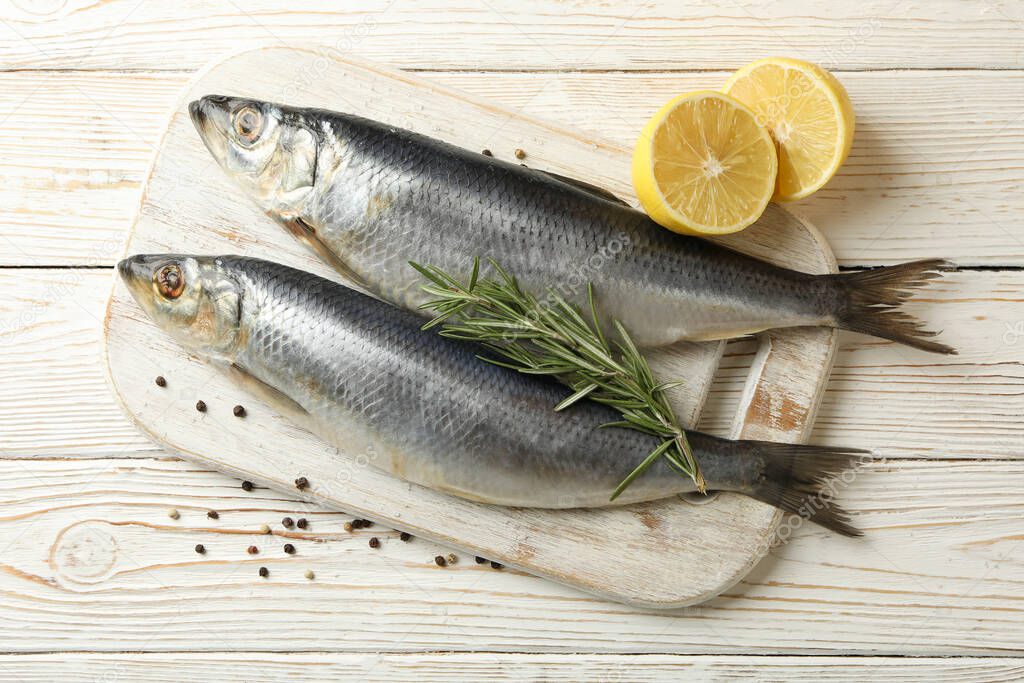 Board with fresh herring fish and spices on white wooden background