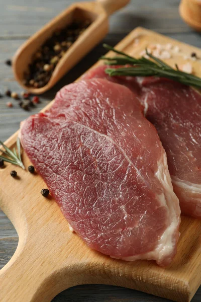 Ahşap zemin üzerinde çiğ biftek, ot ve baharat bulunan bir pano.