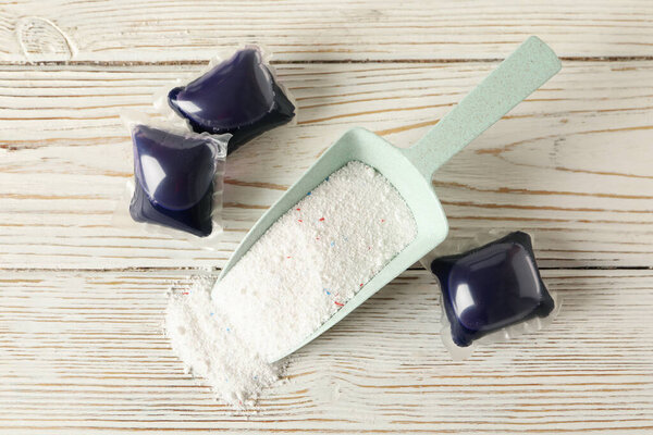 Scoop with washing powder and laundry capsules on white wooden background