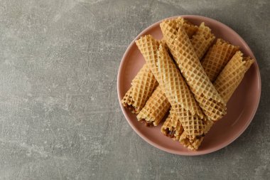 Gri zemin üzerinde yoğunlaştırılmış süt bulunan gofret ruloları ile tabak