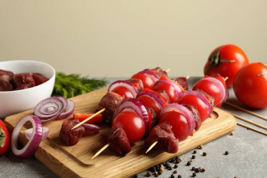 Gri arkaplanda çiğ şiş kebabı ve malzemeleri olan tahta