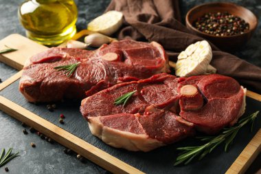 Siyah dumanlı arka planda çiğ et, ot ve baharat bulunan bir pano.