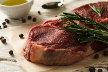 Ahşap zemin üzerinde çiğ biftek, ot ve baharat bulunan kağıt fırını.