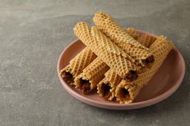 Gri zemin üzerinde yoğunlaştırılmış süt bulunan gofret ruloları ile tabak