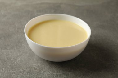 Gri arka planda yoğunlaştırılmış sütle birlikte kase