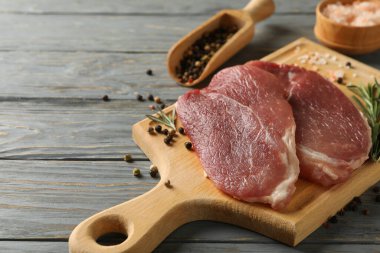 Ahşap zemin üzerinde çiğ biftek, ot ve baharat bulunan bir pano.