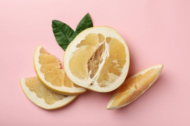 Pomelo meyvesinin yarısı, pembe arka planda dilimler ve yapraklar