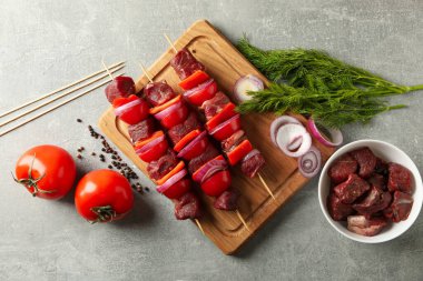 Gri arkaplanda çiğ şiş kebabı ve malzemeleri olan tahta