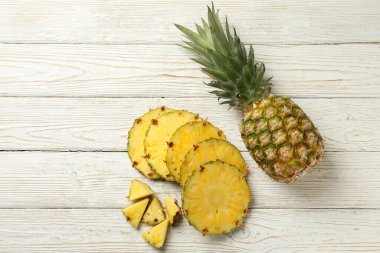 Beyaz ahşap arka planda ananas ve dilimler.