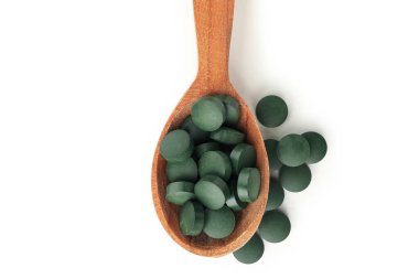 Beyaz arka planda izole edilmiş spirulina hapları olan tahta kaşık.
