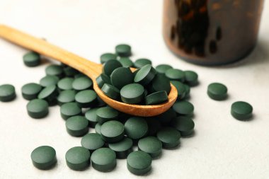 Beyaz desenli arka planda spirulina hapları bulunan şişe ve ahşap kaşık.