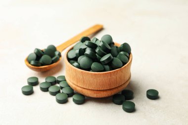 Beyaz desenli arka planda spirulina haplarıyla ahşap kase ve kaşık.