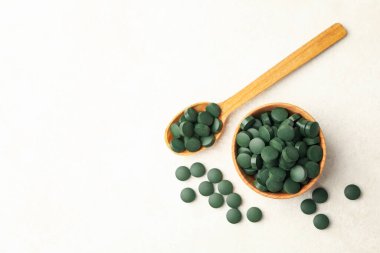 Beyaz desenli arka planda spirulina haplarıyla ahşap kase ve kaşık.