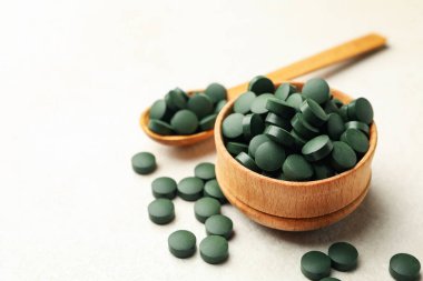 Beyaz desenli arka planda spirulina haplarıyla ahşap kase ve kaşık.