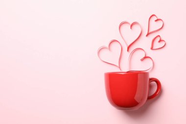 Kırmızı bardak ve pembe arka planda dekoratif kalpler.