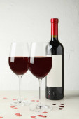 Láhev a sklenice červeného vína na bílém tvarovaném stole