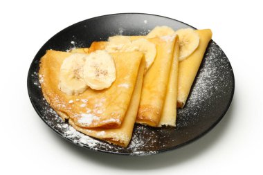 Beyaz zemin üzerinde şeker tozu ve muz dilimleri olan bir tabak krep.