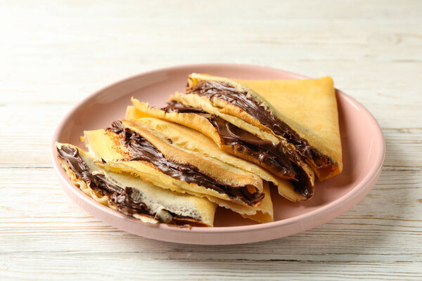 Plate of crepes with chocolate paste on white wooden background