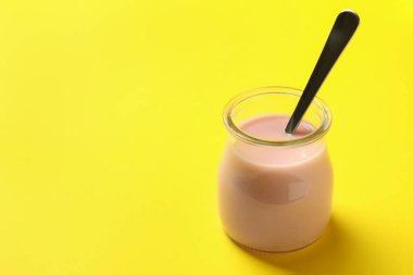 Sarı arka planda kaşık ve yoğurt dolu cam kavanoz.