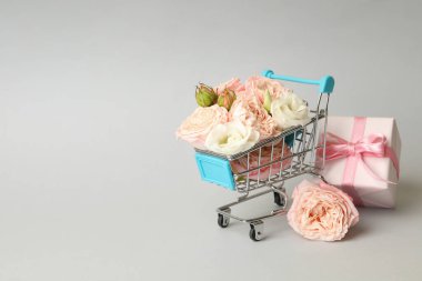 Gül dolu alışveriş arabası ve gri arka planda hediye kutusu, metin için yer