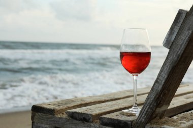 Kumlu deniz sahilinde bir bardak şaraplı ahşap bank.