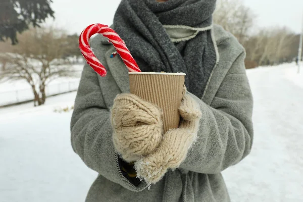Woman in mittens hold cup of hot drink outdoor in winter