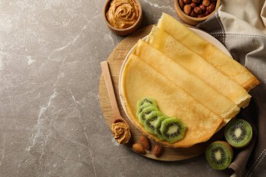 Kahvaltıda krep, kivi, fıstık ezmesi ve fındık ve gri arka planda.